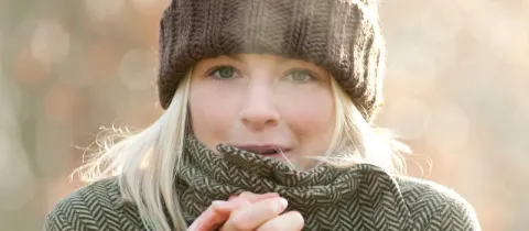 Gros plan sur une femme blonde souriante, emmitouflée dans un bonnet et une écharpe.