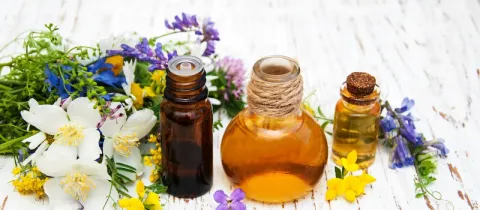 Bouteilles d'huiles essentielles ou végétales entourées de fleurs et d'herbes sur une table en bois.