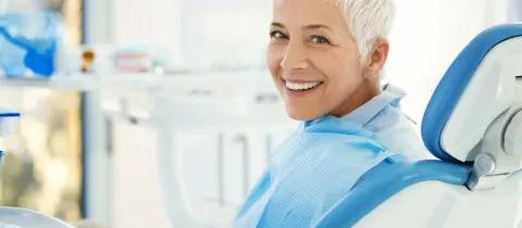 Une femme souriante aux cheveux courts gris dans un fauteuil de dentiste.
