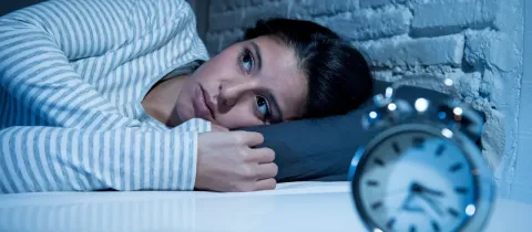 Une femme aux yeux ouverts est allongée dans son lit la nuit, observant un réveil, souffrant d'insomnie.
