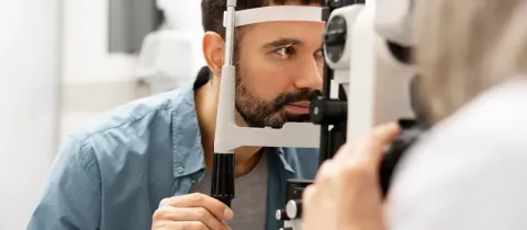 Un homme barbu fixe un appareil d'examen oculaire pendant un examen ophtalmologique.