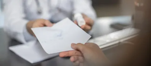 Un médecin remet une ordonnance ou des documents médicaux à un patient assis.