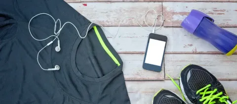 Une composition d'articles de sport : un t-shirt, un téléphone avec écouteurs, une bouteille et une paire de baskets.