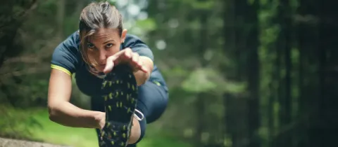 Une femme en tenue de sport s'étire en forêt, posant son pied sur une bûche, se concentrant sur l'exercice.