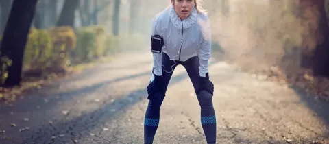 Une coureuse s'arrête pour reprendre son souffle sur un chemin, penchée en avant, les mains sur les genoux, par temps froid.