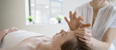 Une praticienne en médecine douce effectue une séance d'acupuncture sur le front d'une patiente allongée.
