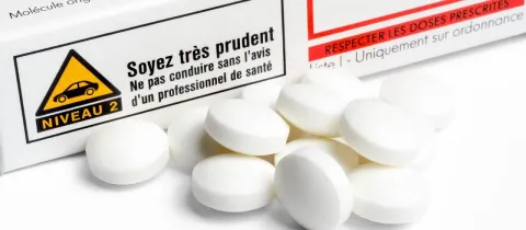 Un tas de comprimés blancs ronds devant une boîte de médicament française avec mentions légales et avertissement.