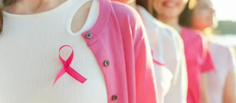 Plusieurs femmes portant des rubans roses de sensibilisation au cancer du sein, souriant, focus sur la première.