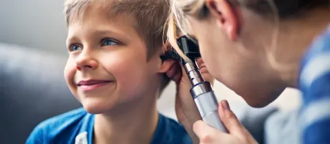 Un médecin examine l'oreille d'un jeune garçon souriant à l'aide d'un otoscope.