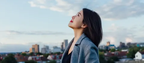 Une jeune femme regarde le ciel avec optimisme en milieu urbain, profitant d'un moment de calme.