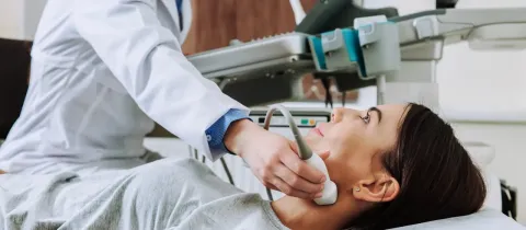 Un médecin effectue une échographie du cou sur une patiente allongée, à l'aide d'un appareil d'imagerie médicale.