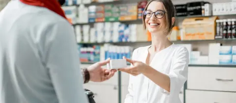 Une pharmacienne souriante tend une boîte de médicament à un client à l'officine.
