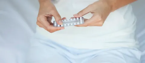 Gros plan sur les mains d'une femme sortant une pilule contraceptive d'une plaquette.