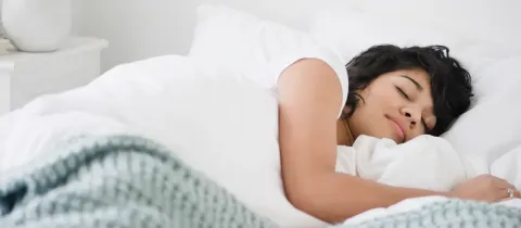 Une jeune femme dort paisiblement sous une couverture blanche et verte dans un lit confortable.