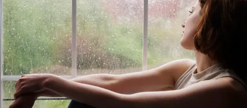 Femme pensive regardant par la fenêtre un jour de pluie.