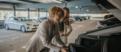 Deux femmes en tenue professionnelle rangent leurs valises dans une voiture.