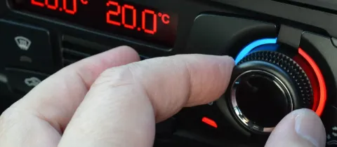 Gros plan d'une main ajustant un cadran de climatisation automobile affichant 20.0°C en rouge.