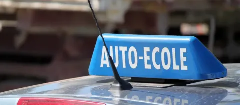Gros plan d'un panneau bleu "AUTO-ECOLE" sur le toit d'une voiture, indiquant un véhicule d'auto-école.