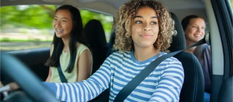 Une femme souriante au volant, avec deux passagères en arrière-plan, lors d'un trajet en covoiturage.