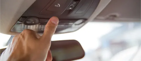 Un doigt appuie sur le bouton "SOS" du panneau de commande au plafond d'une voiture.