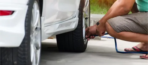 Une personne accroupie vérifie la pression et gonfle un pneu de voiture blanc.