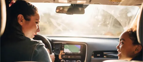 Deux personnes, une femme au volant et une jeune fille à l'arrière, discutent joyeusement dans une voiture.