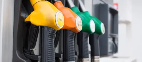 Gros plan sur plusieurs pistolets de différentes couleurs (jaune, orange, vert) à une pompe à essence.