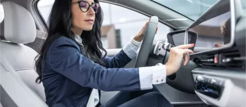 Une femme d'affaires dans une voiture moderne, consultant son tableau de bord avec concentration.