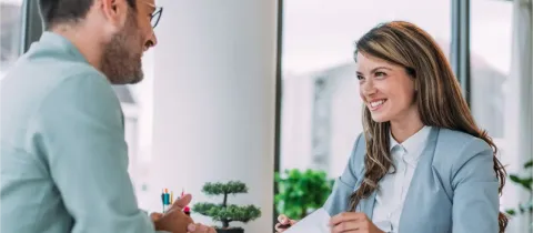 Une conseillère avec des documents discute avec un homme assis à un bureau.