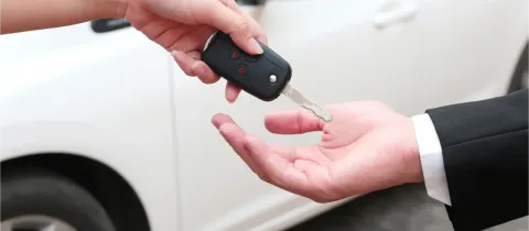 Une main tend une clé de voiture à une autre main, devant une voiture blanche.