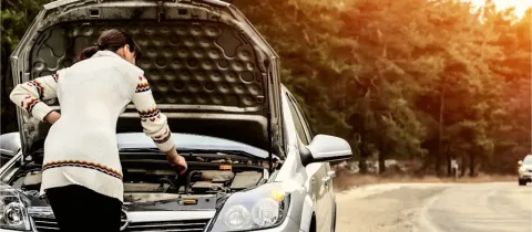 Une femme regarde sous le capot ouvert d'une voiture en panne sur le bord de la route.