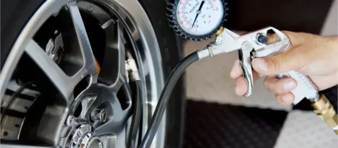 Une main gonfle un pneu de voiture avec un pistolet de gonflage et un manomètre sur une jante chromée.