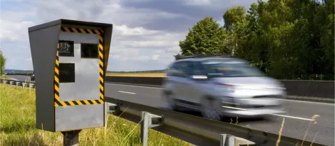 Un radar de vitesse gris et jaune sur le bord d'une autoroute, avec une voiture floue en mouvement.