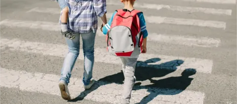 Une femme et un enfant traversent une route sur un passage piéton en plein soleil.