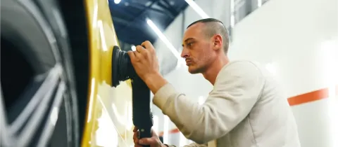 Un homme travaille méticuleusement sur la carrosserie d'une voiture jaune avec une polisseuse.