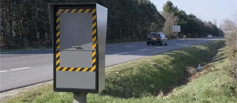Un radar automatique français avec des bandes jaunes et noires au bord d'une route.