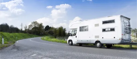 Un grand camping-car blanc roule sur une route sinueuse à travers la campagne, sous un ciel bleu parsemé de nuages blancs.
