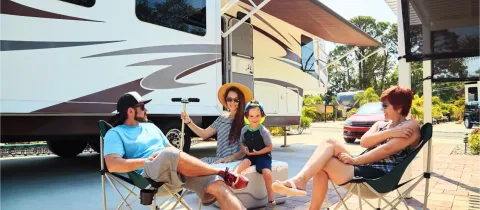 Une famille avec un jeune enfant se détend à l'extérieur de leur camping-car sous un auvent par une journée ensoleillée.