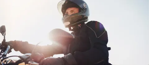 Un motard en tenue de protection et casque intégral regarde vers le ciel sous un soleil éclatant.