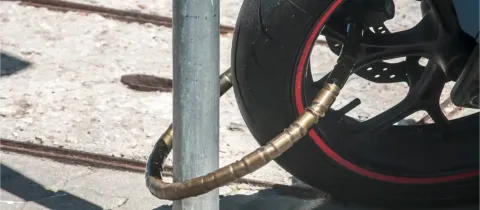 Gros plan d'une chaîne antivol enroulée autour de la roue avant d'une moto et d'un poteau.