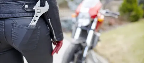 Vue arrière d'une femme en pantalon de cuir avec une clé à molette dans la poche, près d'une moto.