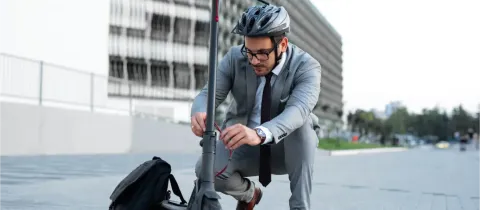 Un homme en costume et casque ajuste sa trottinette électrique dans un environnement urbain moderne.