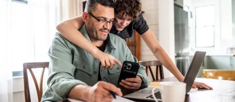 Un père travaille à la maison avec son fils consultant son téléphone.