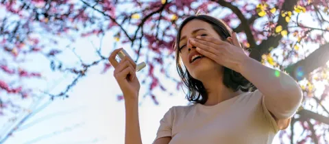 Une femme utilise un inhalateur sous un arbre en fleurs.