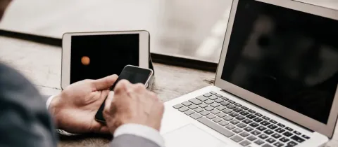 Gros plan sur les mains d'un homme en costume, utilisant un smartphone à côté d'une tablette et d'un ordinateur portable.