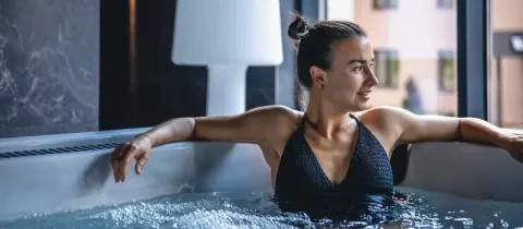 Femme souriante se détendant dans un jacuzzi ou un bain à remous, profitant d'un moment de relaxation en intérieur.