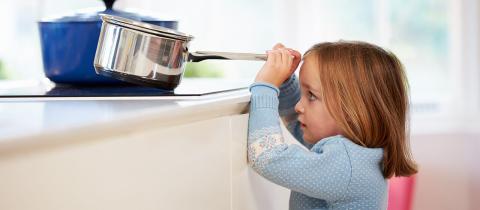 Une enfant saisit une casserole d'eau bouillante sur le comptoir, s'exposant à un danger de brûlure.
