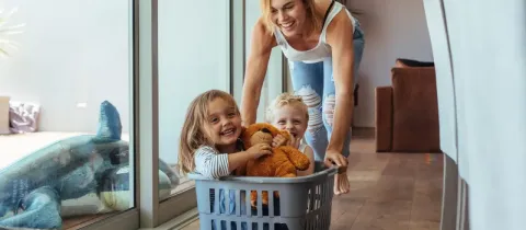Une mère s'amuse à pousser ses deux jeunes enfants installés dans un panier à linge au milieu du salon.