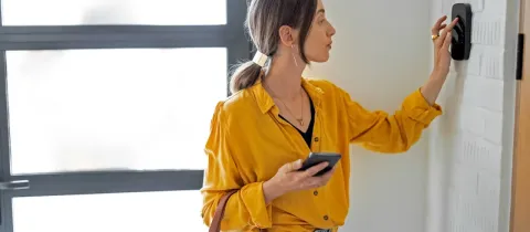Femme moderne utilisant une borne de contrôle de porte ou de sécurité à l'entrée d'une maison lumineuse.