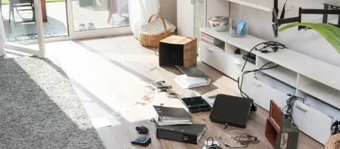 Pièce d'une maison après un cambriolage, avec des dossiers, des papiers et des objets éparpillés sur le sol.